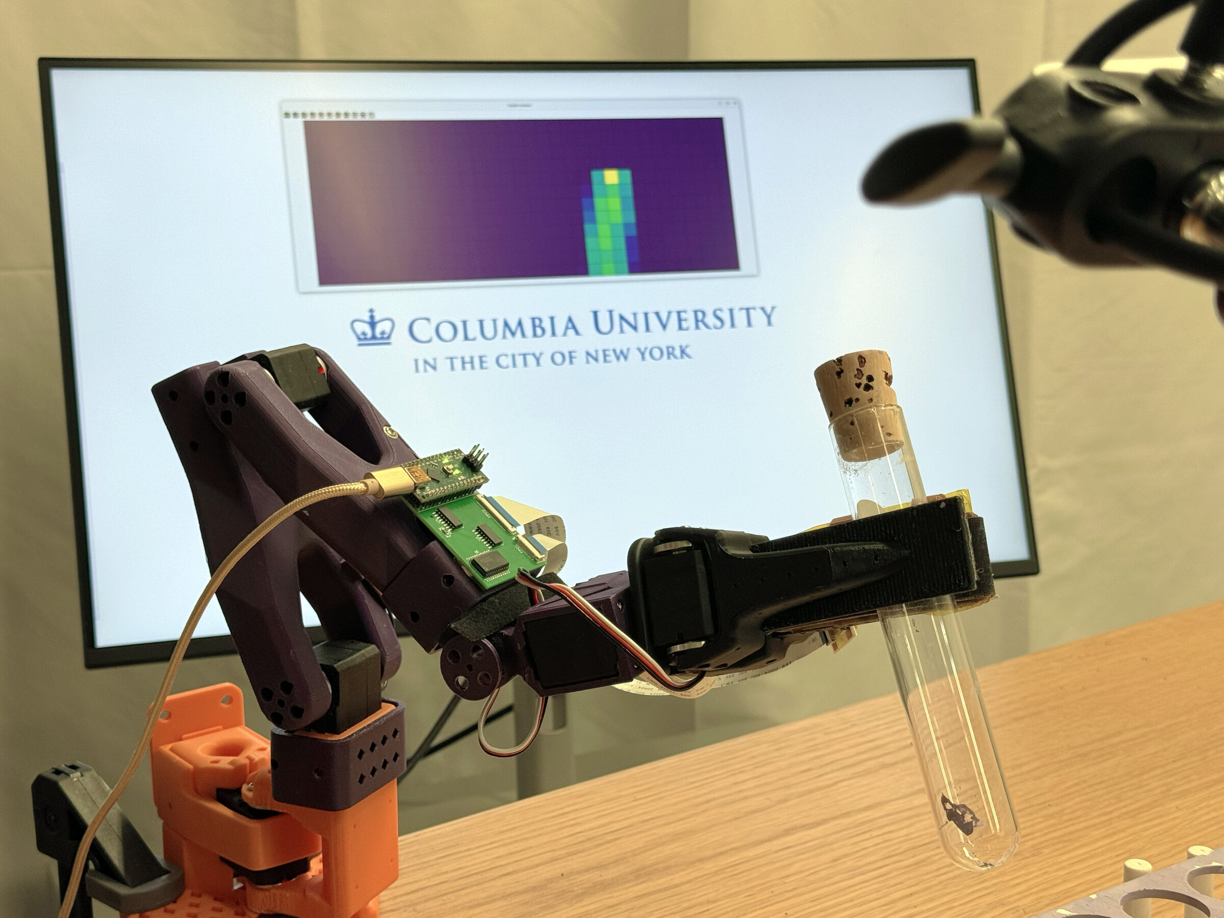LeFlexiTac tactile robot gripper holding a test tube in front of a Columbia University display